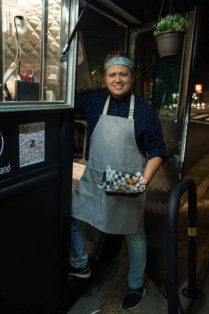 A smiling food truck vendor serving delicious street food at night.